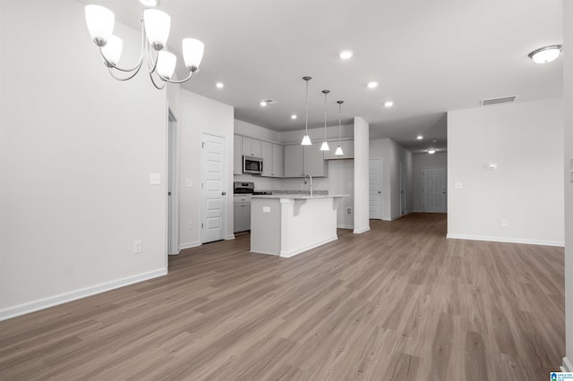 kitchen with a breakfast bar area, appliances with stainless steel finishes, hanging light fixtures, a center island, and light hardwood / wood-style floors