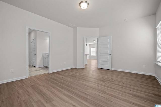 unfurnished bedroom featuring ensuite bathroom and light hardwood / wood-style flooring