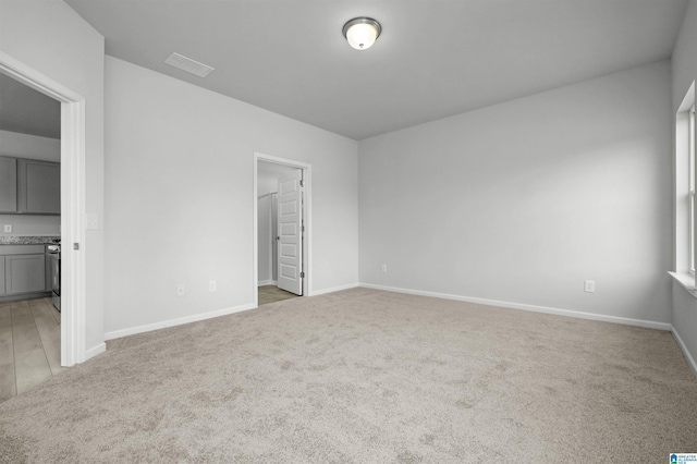 unfurnished bedroom with ensuite bathroom, a walk in closet, and light carpet