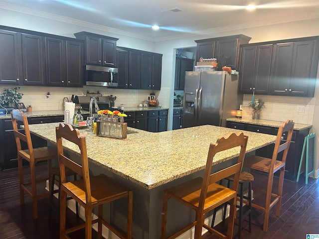 kitchen featuring a kitchen island with sink, backsplash, a breakfast bar area, and stainless steel appliances