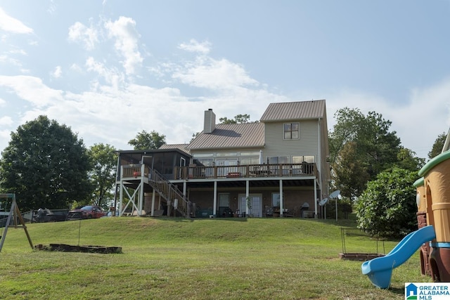 rear view of property featuring a deck, a lawn, a chimney, and a sunroom