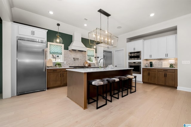 kitchen with an island with sink, stainless steel appliances, custom range hood, and decorative backsplash