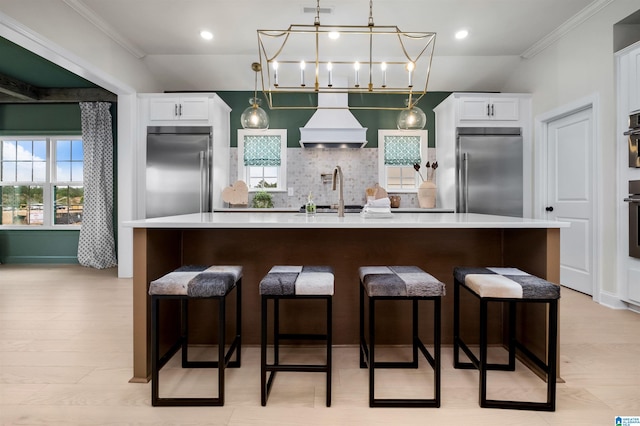 kitchen with high end fridge, premium range hood, stainless steel built in fridge, and white cabinetry