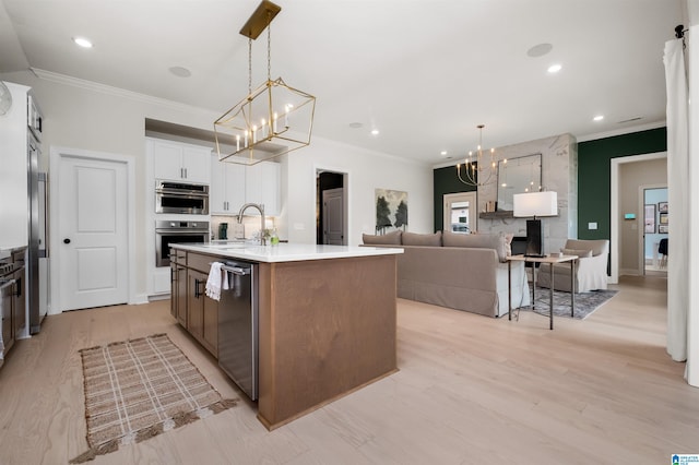 kitchen with light wood-type flooring, pendant lighting, stainless steel appliances, an island with sink, and white cabinetry