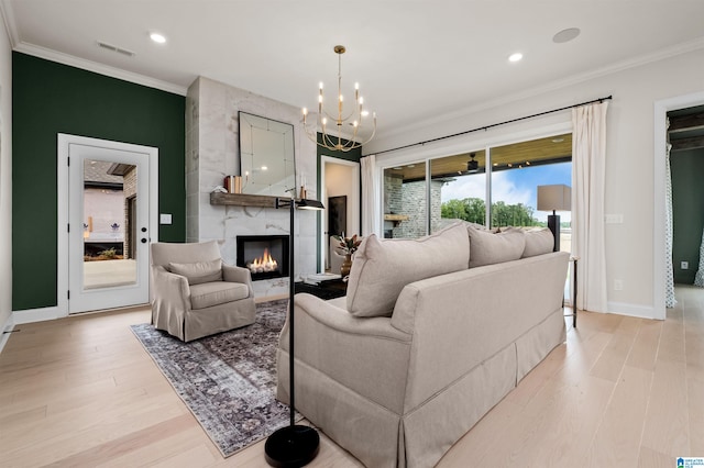 living room with a notable chandelier, light wood-type flooring, a premium fireplace, and ornamental molding