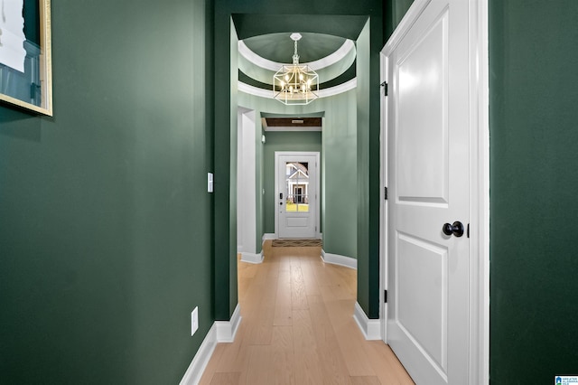 hallway featuring light hardwood / wood-style flooring, a tray ceiling, ornamental molding, and a notable chandelier