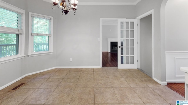 spare room featuring a chandelier, light tile patterned flooring, a fireplace, visible vents, and crown molding