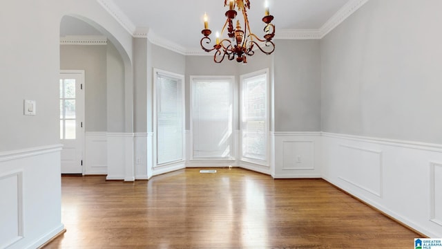 unfurnished dining area featuring ornamental molding, arched walkways, a wealth of natural light, and wood finished floors