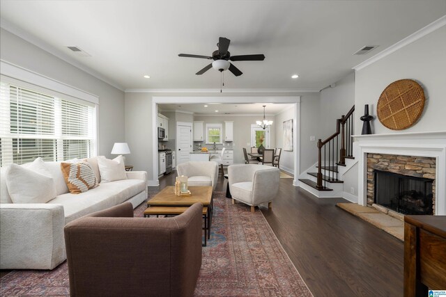 living room with dark wood-type flooring, a fireplace, ornamental molding, and ceiling fan with notable chandelier