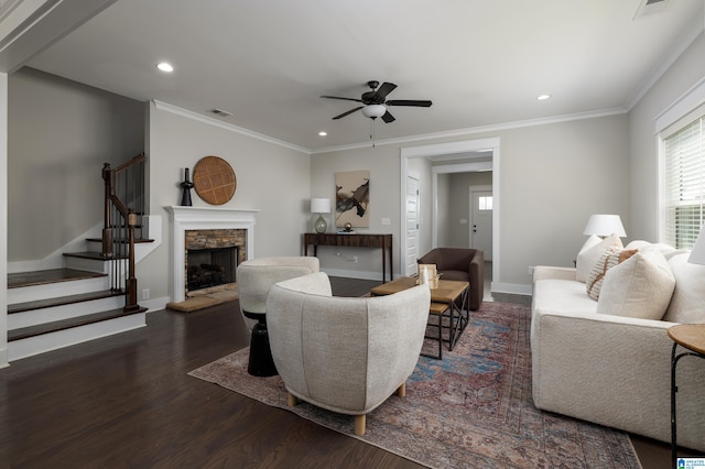 living room featuring a stone fireplace, ornamental molding, dark wood-type flooring, and ceiling fan