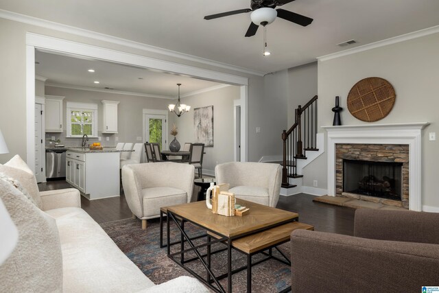 living room with ceiling fan with notable chandelier, a stone fireplace, wood-type flooring, sink, and ornamental molding