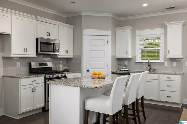 kitchen with white cabinetry, appliances with stainless steel finishes, dark wood-type flooring, a center island, and tasteful backsplash