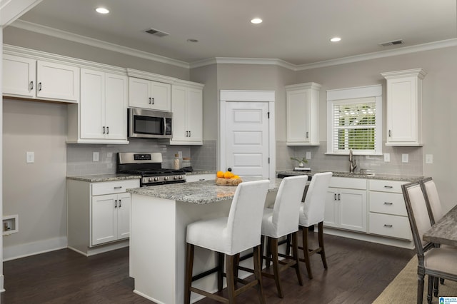 kitchen with appliances with stainless steel finishes, white cabinetry, a kitchen island, and dark hardwood / wood-style floors