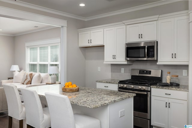 kitchen with appliances with stainless steel finishes, white cabinets, ornamental molding, a center island, and light stone countertops