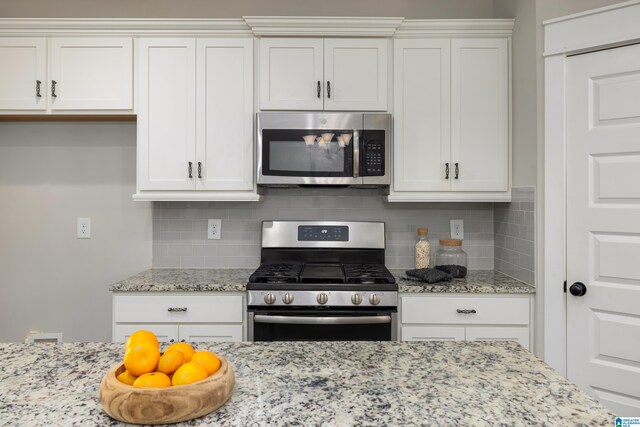 kitchen with appliances with stainless steel finishes, light stone counters, white cabinets, and decorative backsplash