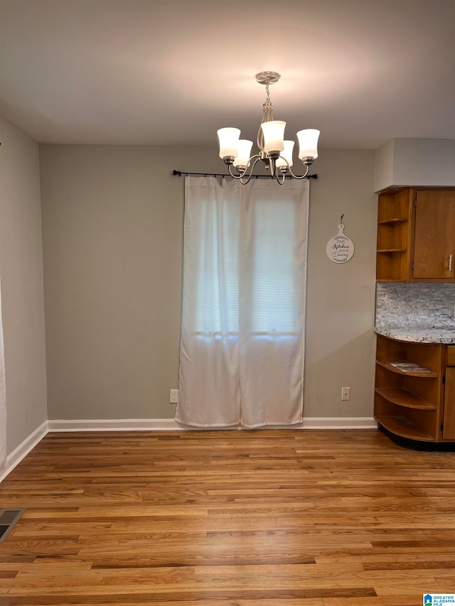 unfurnished dining area featuring an inviting chandelier and light hardwood / wood-style flooring