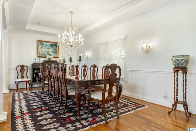 dining space with an inviting chandelier, a tray ceiling, ornamental molding, and hardwood / wood-style flooring