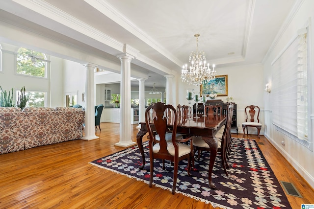 dining room featuring ornamental molding, wood-type flooring, a tray ceiling, and ornate columns