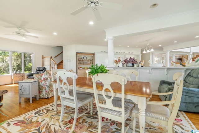 dining space featuring ornate columns, ceiling fan with notable chandelier, and light wood-type flooring