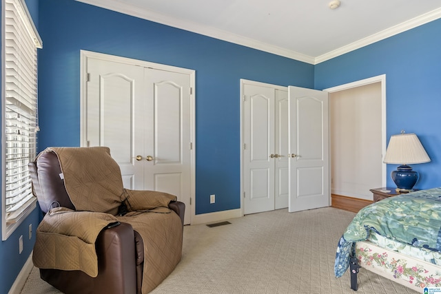 bedroom with crown molding, two closets, and light carpet