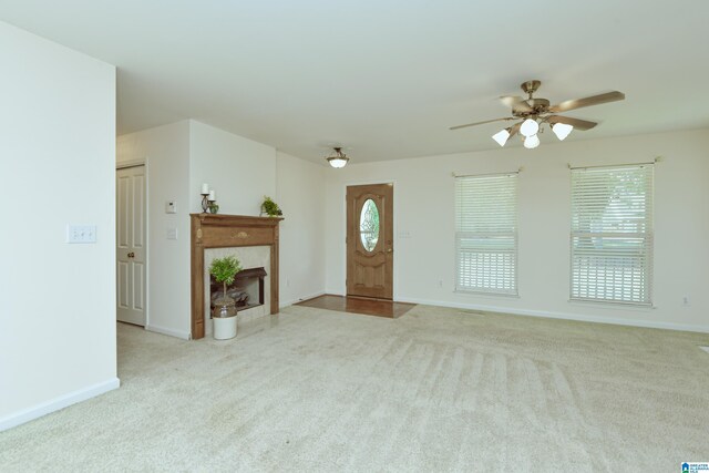 unfurnished living room featuring ceiling fan, a tile fireplace, and light colored carpet