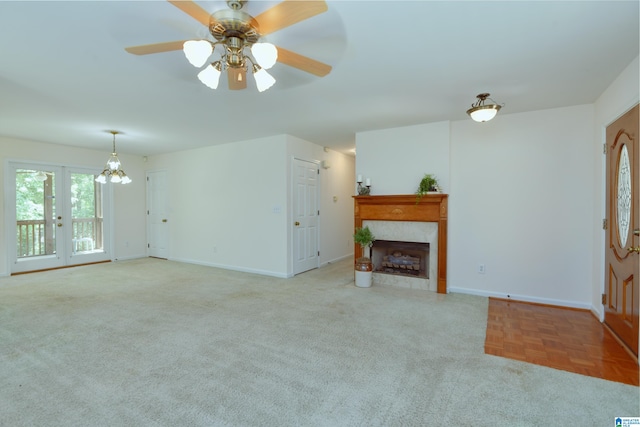 unfurnished living room featuring ceiling fan, a tiled fireplace, french doors, and light carpet