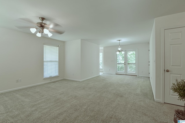 carpeted spare room featuring ceiling fan with notable chandelier