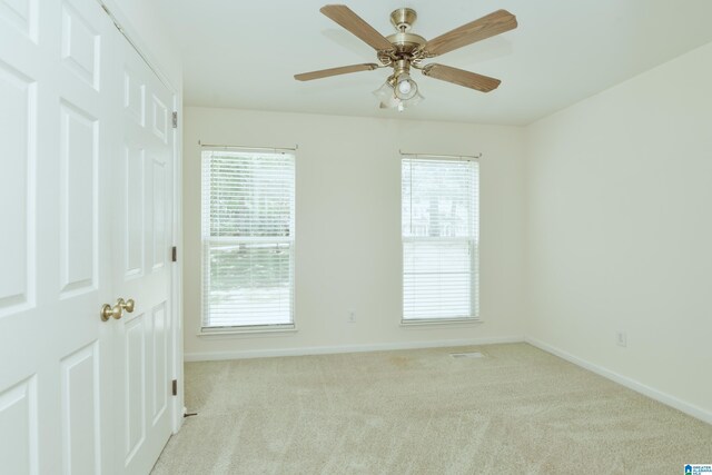 empty room featuring a wealth of natural light, light carpet, and ceiling fan