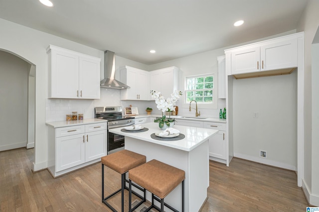 kitchen featuring decorative backsplash, hardwood / wood-style floors, wall chimney exhaust hood, electric range, and a kitchen island