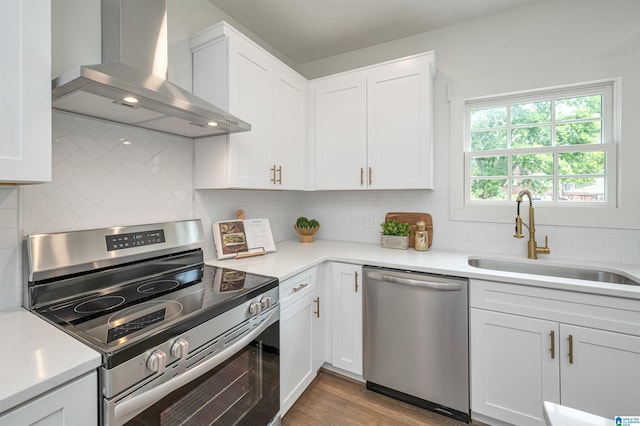 kitchen with sink, light wood-type flooring, appliances with stainless steel finishes, decorative backsplash, and wall chimney range hood