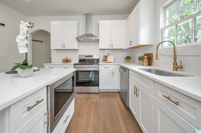 kitchen featuring wall chimney range hood, sink, light hardwood / wood-style flooring, white cabinetry, and stainless steel appliances