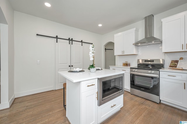 kitchen with built in microwave, stainless steel electric stove, wall chimney range hood, and white cabinetry