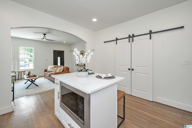 kitchen with stainless steel microwave, white cabinetry, a kitchen breakfast bar, a center island, and a barn door