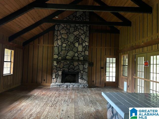 unfurnished living room with a wealth of natural light, a stone fireplace, lofted ceiling with beams, and wood finished floors