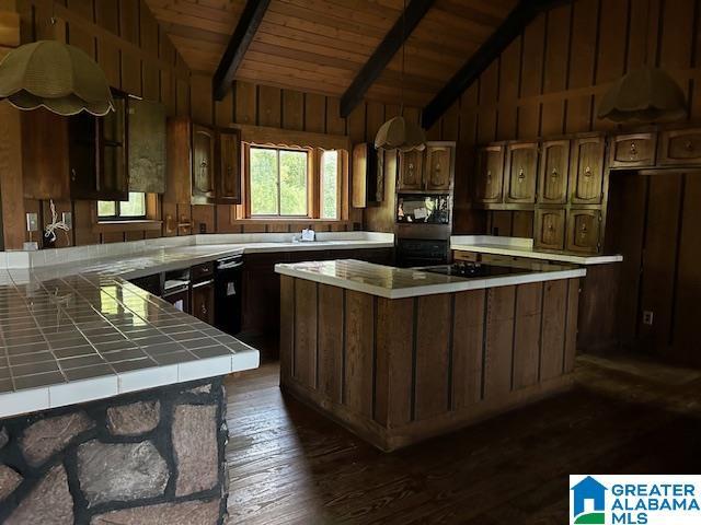 kitchen with vaulted ceiling with beams, dark wood-style flooring, tile counters, a center island, and black appliances