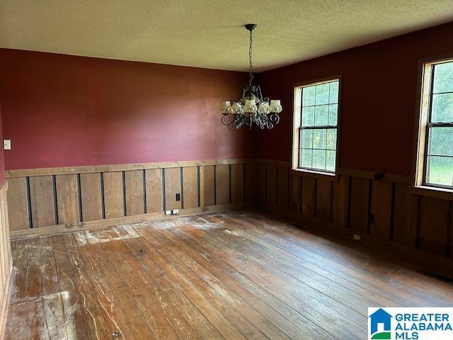 unfurnished dining area with plenty of natural light, hardwood / wood-style floors, wainscoting, and a notable chandelier