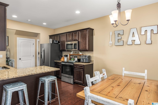 kitchen with a kitchen bar, light stone counters, dark wood-style floors, stainless steel appliances, and dark brown cabinetry