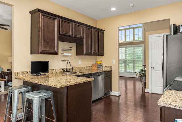 kitchen featuring light stone countertops, dark wood finished floors, a sink, stainless steel appliances, and dark brown cabinets