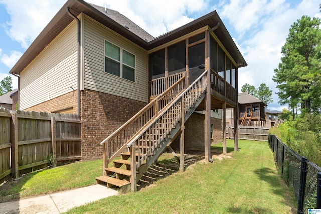 back of property featuring a lawn, a fenced backyard, a sunroom, brick siding, and stairs