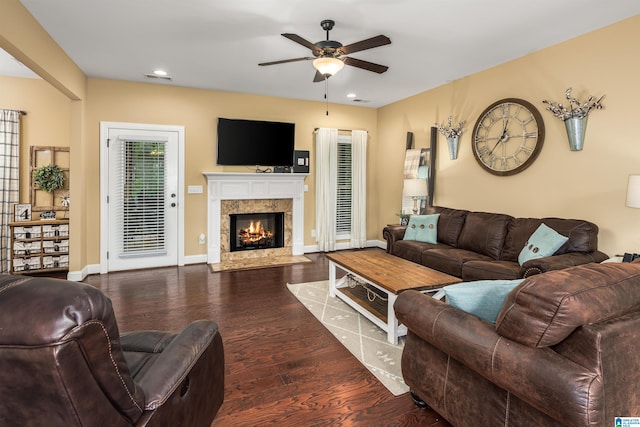 living room with a tiled fireplace, ceiling fan, and dark wood-type flooring