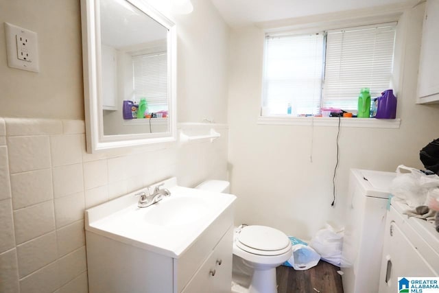 bathroom with tile walls, vanity, washer and clothes dryer, and toilet