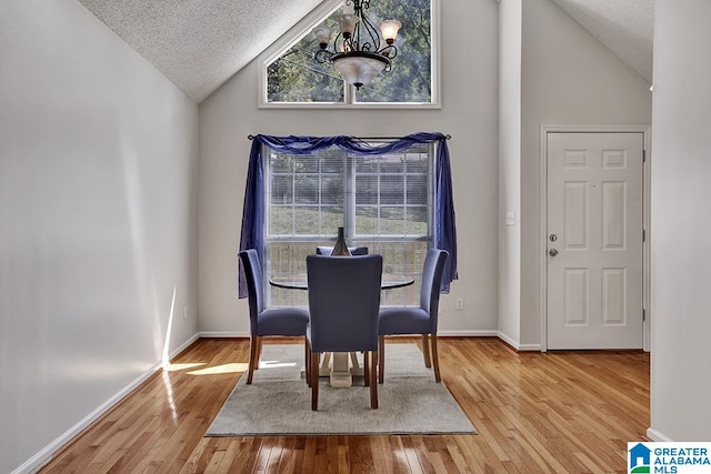 dining room with a textured ceiling, light hardwood / wood-style flooring, vaulted ceiling, and a chandelier