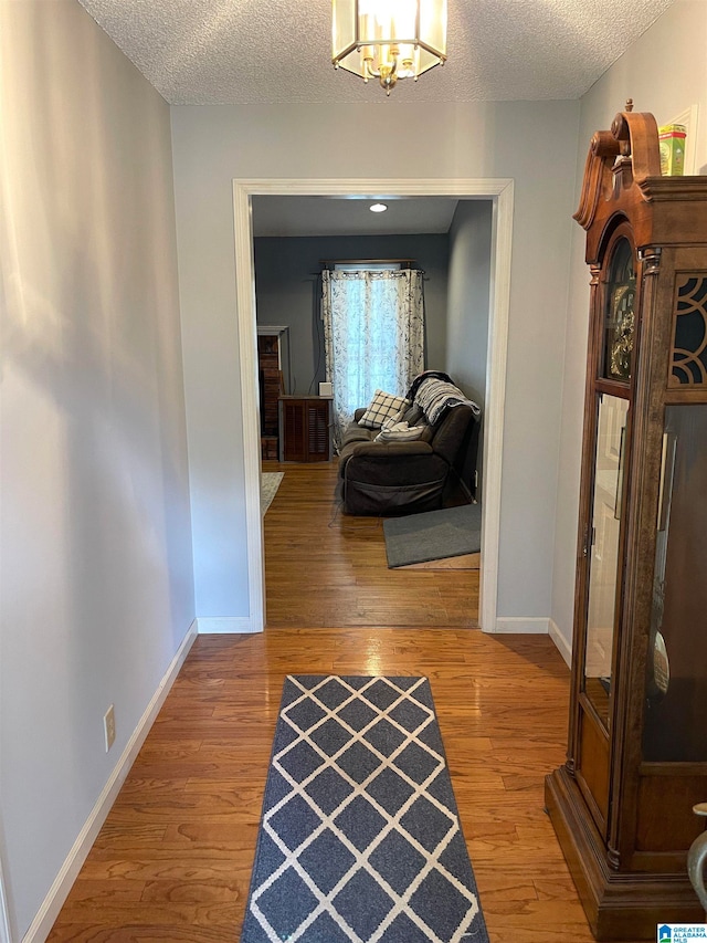 hallway featuring hardwood / wood-style flooring, a textured ceiling, and a chandelier