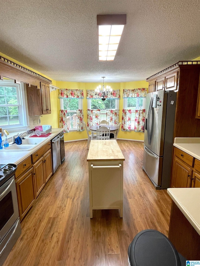 kitchen featuring hardwood / wood-style floors, a notable chandelier, decorative light fixtures, a textured ceiling, and stainless steel appliances