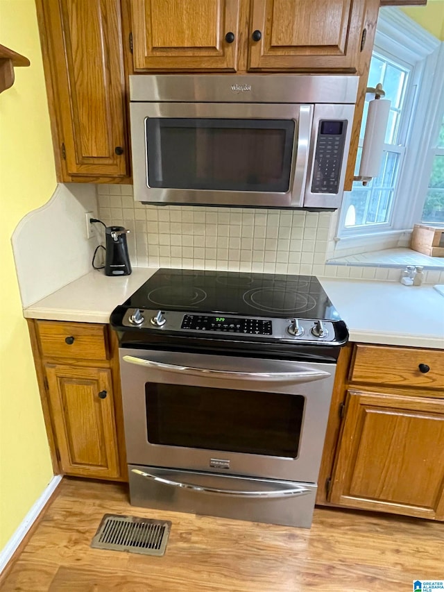 kitchen with appliances with stainless steel finishes, light hardwood / wood-style flooring, and decorative backsplash