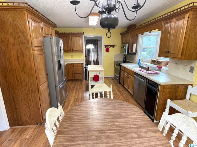 kitchen with backsplash, stainless steel appliances, sink, a notable chandelier, and hardwood / wood-style flooring