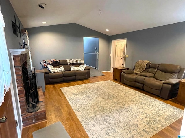 living room featuring light hardwood / wood-style floors, vaulted ceiling, and a brick fireplace