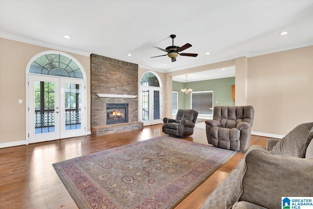 living room featuring french doors, a brick fireplace, ornamental molding, hardwood / wood-style flooring, and ceiling fan with notable chandelier