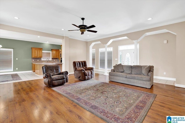 living room with sink, ornate columns, light wood-type flooring, ornamental molding, and ceiling fan