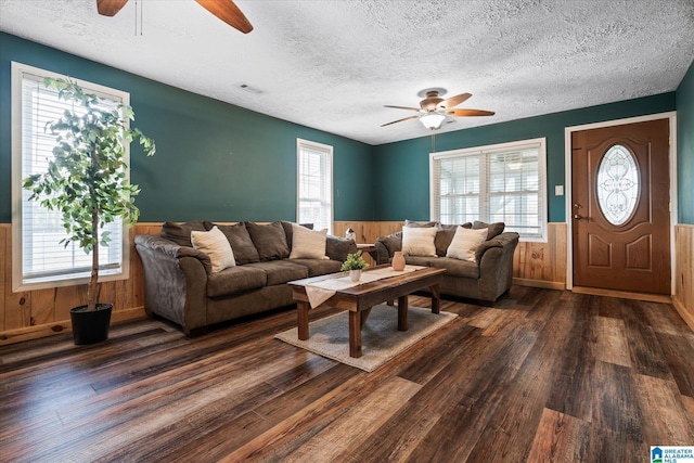 living room featuring dark wood-type flooring, a textured ceiling, ceiling fan, and wood walls